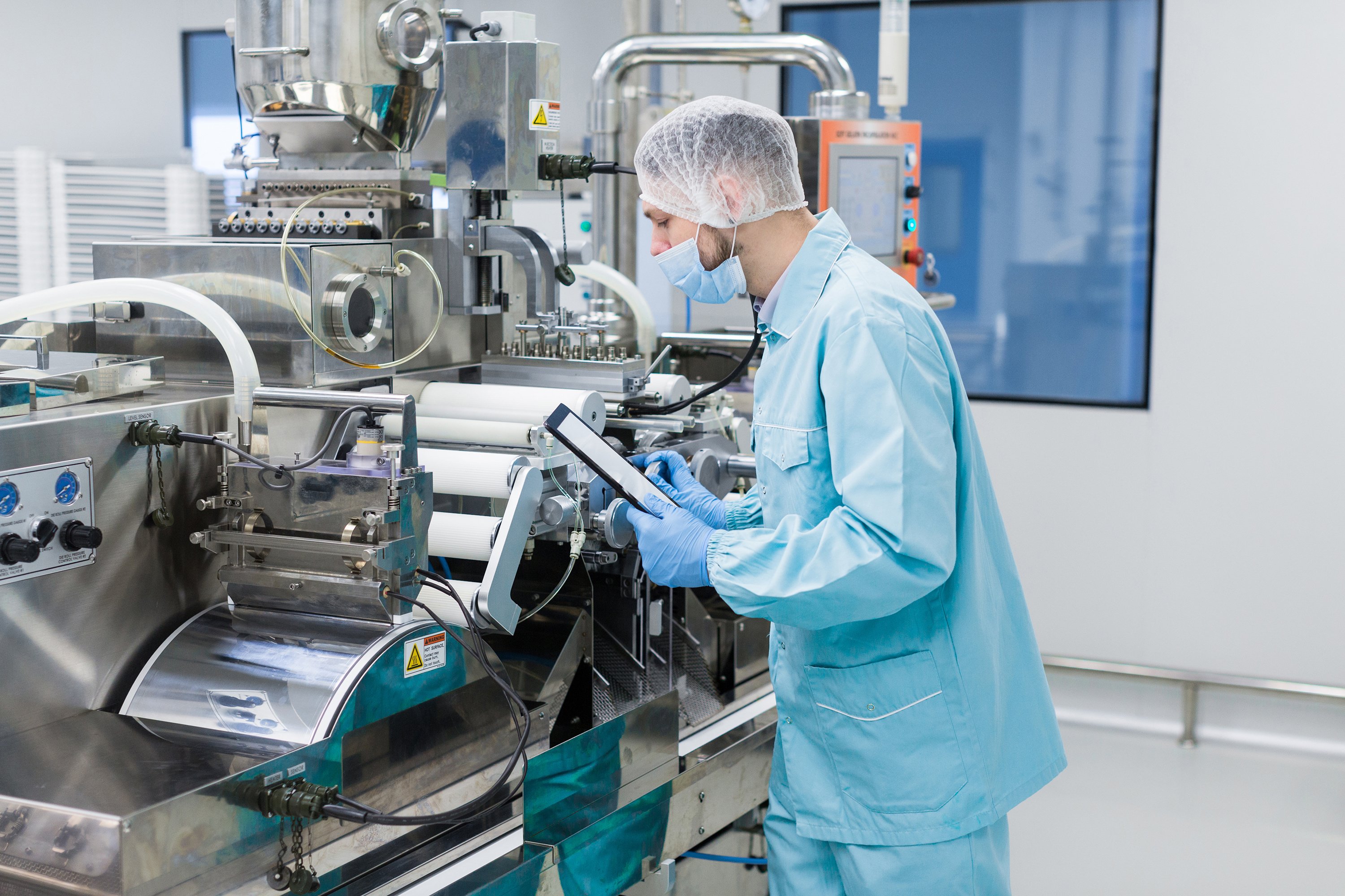 caucasian-scientist-blue-lab-uniform-configure-manufacture-machine-with-shafts-control-panel-checking-readings-making-notes copy-1